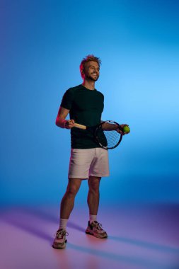 Çekici bir gülümsemesi olan genç bir adam, bir tenis raketi ve topunu sanatsal bir zemine karşı tutuyor..