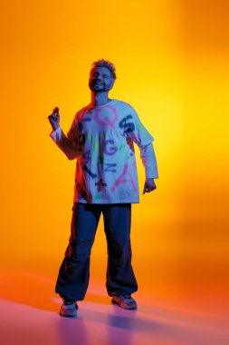 Yakışıklı genç adam sanatsal enerjiyle dolu parlak, renkli bir ortamda neşeyle dans ediyor..