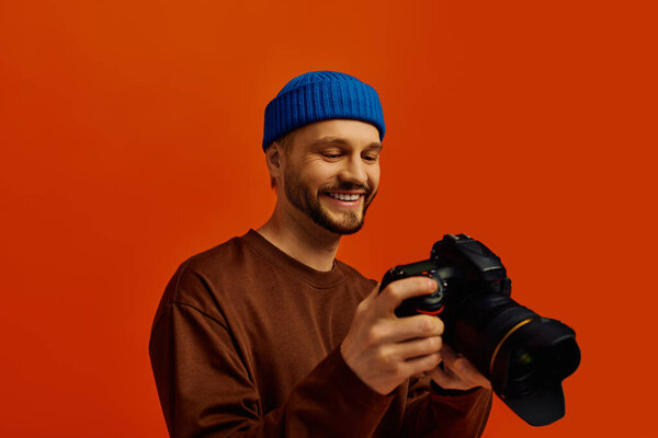 Handsome young man smiles brightly while holding a camera, ready to capture joyful moments.