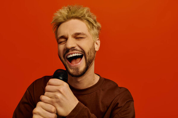 A handsome young man is gleefully singing while holding a microphone and smiling brightly.