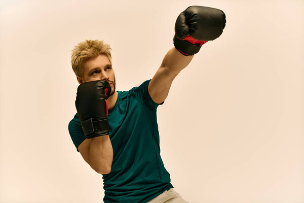 Красивый молодой человек упорно тренируется в боксёрских перчатках, сосредоточенный на своих ударах на простом фоне.