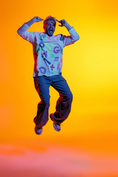 Energetic young man jumps joyfully, expressing happiness against a warm, colorful backdrop.