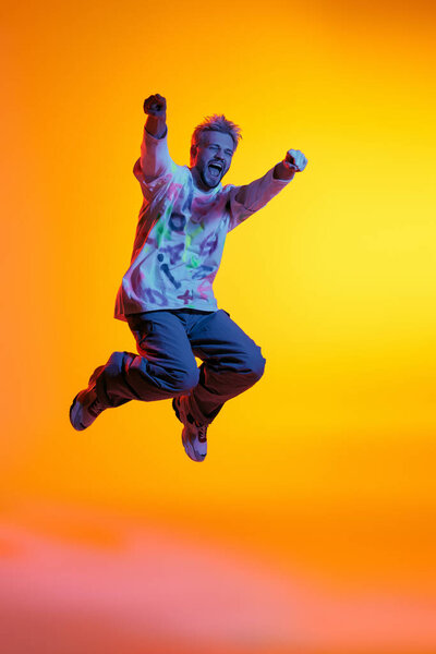 Красивый молодой человек подпрыгивает в воздухе с волнением, обнимая яркий и красочный фон.