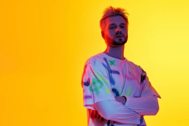 Şık saçlı genç adam cesur sarı bir arka plana karşı özgüvenle poz veriyor, karizmasını gösteriyor..