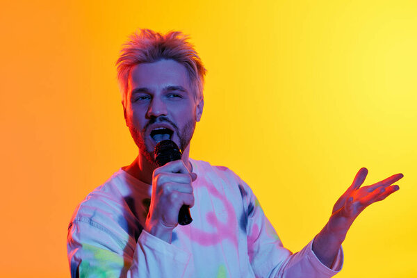 A handsome young man performs energetically with a microphone, surrounded by bright hues.
