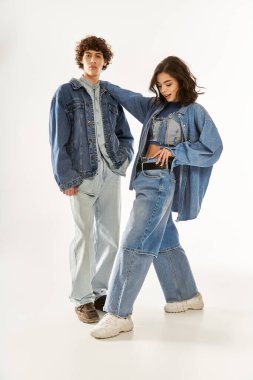 Genç bir çift, modaya uygun kot giysiler içinde birlikte, eğlenceli bir şekilde poz vererek sevgilerini ve tarzlarını ifade ediyor..