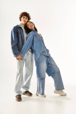 Şık genç çift şık kot giysiler içinde birlikte poz veriyor, sevgi ve neşe sergiliyorlar..