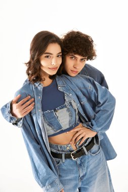 Genç bir çift, modaya uygun kot giysileri sergilerken birbirlerini kucaklıyor, sevgi ve neşe saçıyorlar..