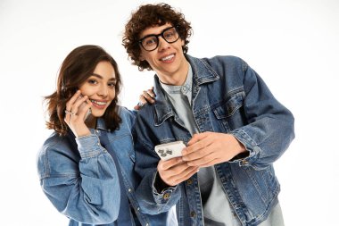 Genç bir çift birlikte gülümsüyor, modaya uygun kotlar giyerken telefonlarını kontrol ediyorlar..