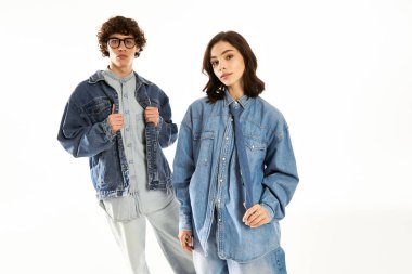 Tarz sahibi erkek ve kadın, beyaz bir arkaplanda eşleşen kot elbiselerle poz verirken aşklarını ifade ederler..