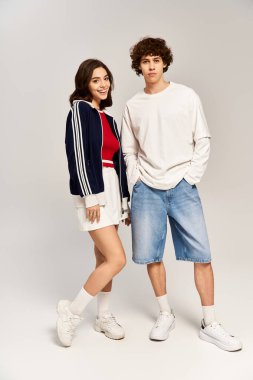 Genç bir çift yan yana durur, son moda kıyafetlerini giyerken aşk ve tarz saçar.