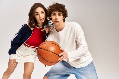 Genç çift basketbol topuyla poz veriyor, modaya uygun kıyafetler giyiyor ve kendilerine güveniyorlar..
