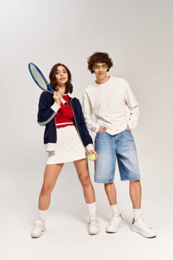 Genç bir çift, kendine güvenerek ayakta duruyor. Tenis kıyafetleri, moda ve romantizmi somutlaştırıyor..