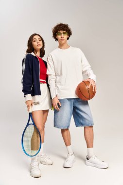 Genç çift, basketbol ve tenis raketiyle güven içinde poz veriyor, tarzlarıyla hava atıyorlar..