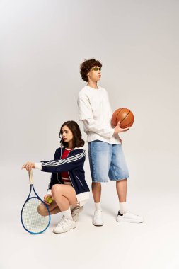 Modern bir stüdyoda şık bir çift atletizm yanlarını basketbol ve tenis takımlarıyla sergiliyor..