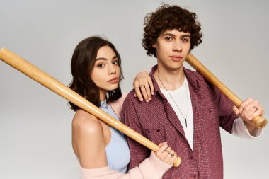 Genç bir çift birbirine yakın duruyor, her biri ahşap bir sopa tutuyor, sevgi ve tarz yayıyorlar..