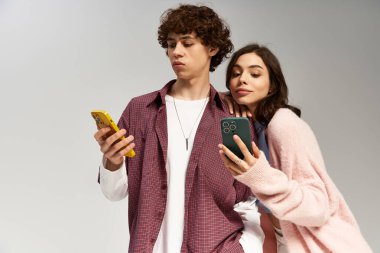 Genç bir çift, akıllı telefonlarına odaklanmış, modern romantizmi gözler önüne seren neşeli bir anı paylaşıyor..