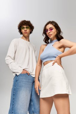 Moda çifti kendine güvenerek poz veriyor, şık kıyafetler ve aksesuarları neşeyle sergiliyor..