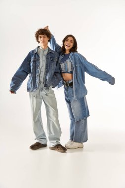 Genç bir çift, parlak bir stüdyoda modaya uygun kot giysiler içinde neşeli pozlar veriyor..