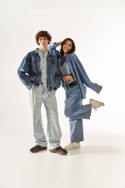 Genç bir çift, aynı kot kıyafetlerini giyerken neşeli pozlar vererek sevgilerini ifade eder..