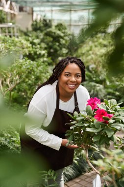 Örgü ören Afrikalı bir Amerikalı kadın neşeyle serada parlak çiçeklere eğilimlidir..