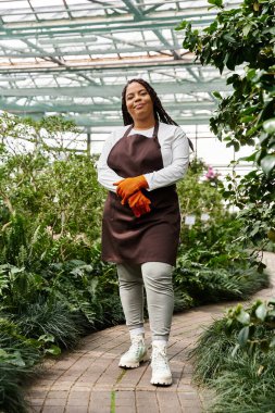 Kendine güvenen, örgülü bir Afrikalı Amerikalı kadın bir serada bitki yetiştiriyor..