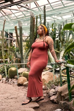 Zarif bir Afrikalı Amerikalı kadın gelişen bitkilerin arasında zarif bir şekilde duruyor, neşe saçıyor..