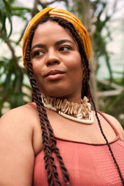 Saçları örgülü güzel bir Afrikalı Amerikalı kadın sera ortamında doğanın güzelliğini kucaklıyor..