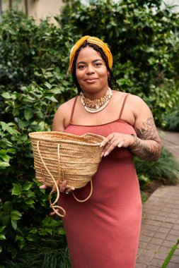 Saçları örgülü neşeli bir Afrikalı Amerikalı kadın, canlı bitkilere daldırılmış bir sepet tutuyor..