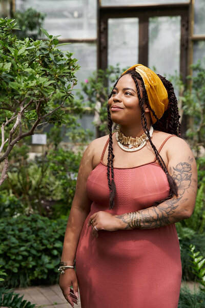 A pretty woman with braids enjoys the tranquil ambiance of a greenhouse surrounded by greenery.