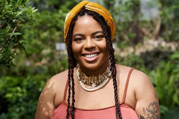 Etrafı gelişen bitkilerle çevriliyken örgü ören neşeli bir Afrikalı Amerikalı kadın..