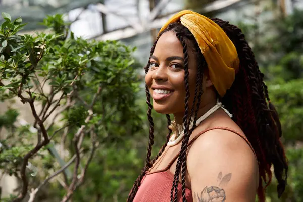 Saçları örgülü neşeli bir Afrikalı Amerikalı kadın seranın ortasında gülümsüyor..