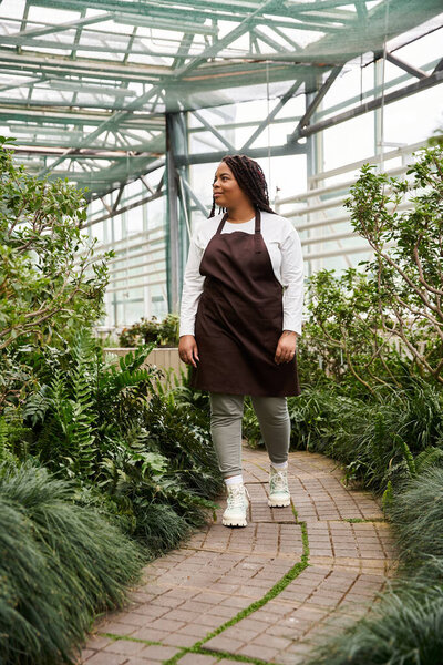 An African American woman tending to lush plants in a serene greenhouse environment.