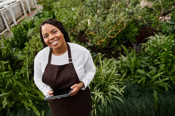 Süslü, mutlu bir bahçıvan yemyeşil alanının yemyeşil bitkileri arasında duruyor..