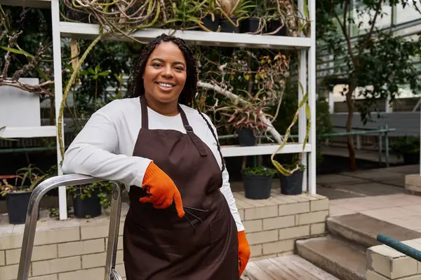 Örgülü Afrikalı bir Amerikalı kadın serada bitki yetiştirirken neşe saçıyor..