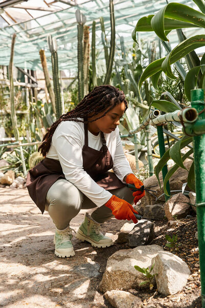 An African American woman tends her plants in a vibrant greenhouse, showcasing her passion.