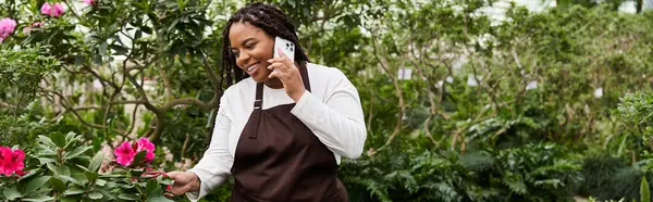 Mutlu bir siyahi kadın, serada canlı çiçeklerle ilgilenirken telefonuyla sohbet eder.