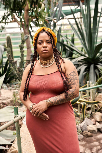 A confident African American woman with braids stands among the thriving plants, radiating bliss.