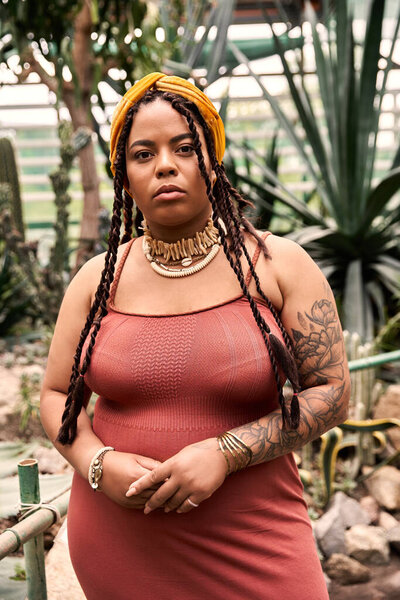 A radiant African American woman stands proudly among lush greenery, exuding bliss and style.