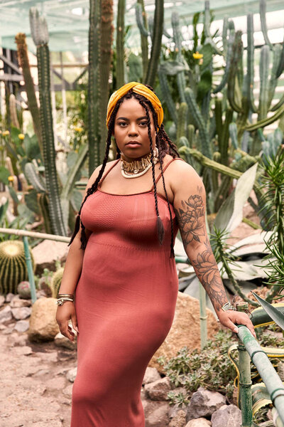 A graceful African American woman with braids shines among tropical plants.