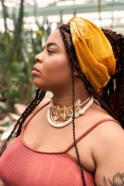 Kendine güvenen, örgülü bir zenci kadın bitkilerle dolu huzurlu bir serada dinleniyor..
