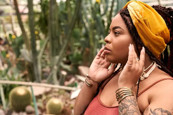 Saçları örgülü neşeli bir Afrikalı Amerikalı kadın yemyeşil bitkilerle çevrili huzurlu bir anın tadını çıkarıyor..