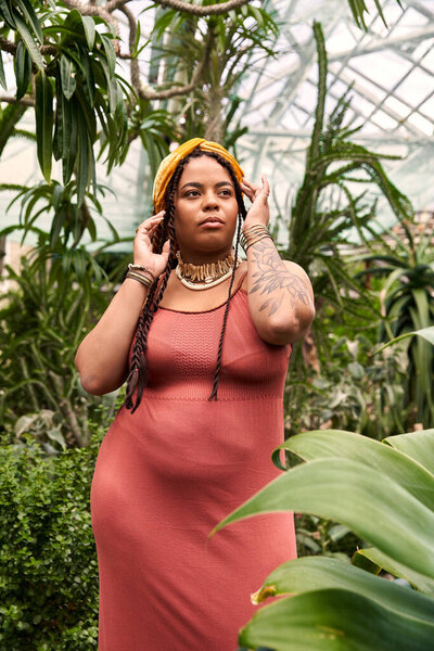 A pretty African American woman with braids enjoys tranquility amidst lush plants in a greenhouse.
