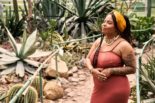 Saçları örgülü neşeli bir kadın yeşil bitkilerin arasında duruyor..