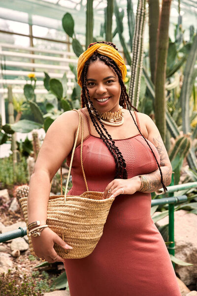 A confident African American woman in a stylish dress enjoys the rich greenery around her.