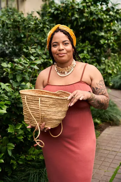 Saçları örgülü neşeli bir Afrikalı Amerikalı kadın, canlı bitkilere daldırılmış bir sepet tutuyor..