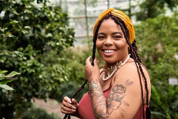 A beautiful African American woman with braids enjoys the greenery in a vibrant greenhouse.