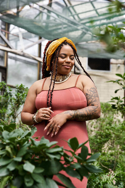 Красивая черная женщина с косичками наслаждается спокойным моментом среди пышных растений в оранжерее.