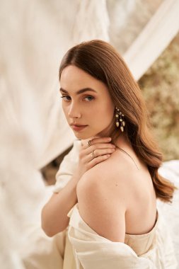 Şık bir genç kadın, yumuşak dokuların arasında eski bir elbise giyerken yansıtır..