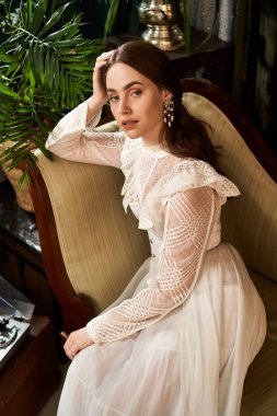 Kaliteli bir elbise giymiş güzel bir kadın şık bir sandalyede oturuyor, büyüleyici bir cazibeyle..